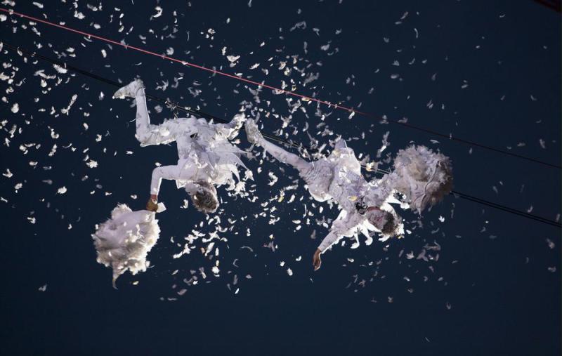 two performers dressed as angels are pillow fighting on a tightrope high above London's Piccadilly Circus